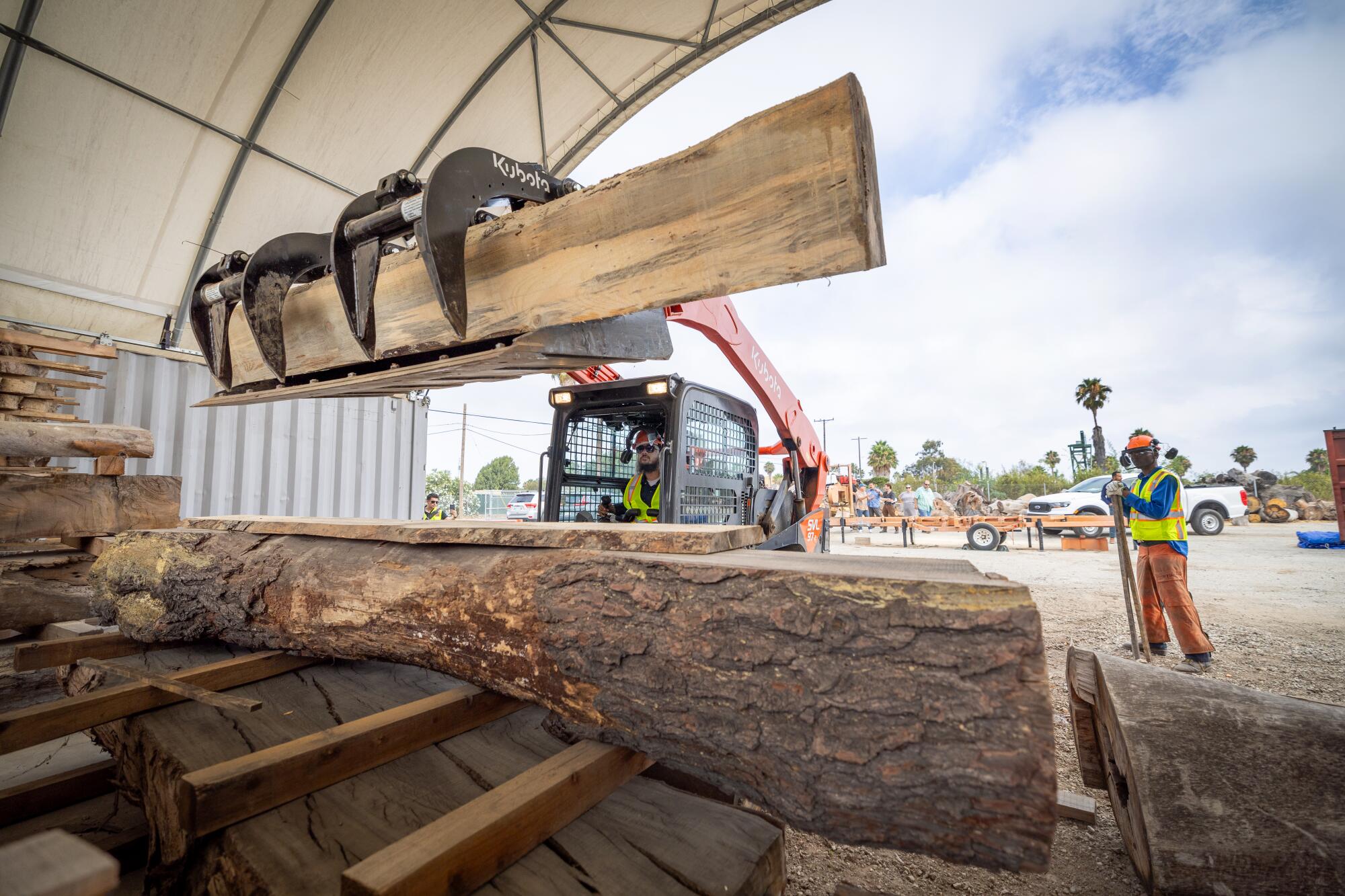 A large piece of wood is stacked at a lumber yard using heavy machinery.