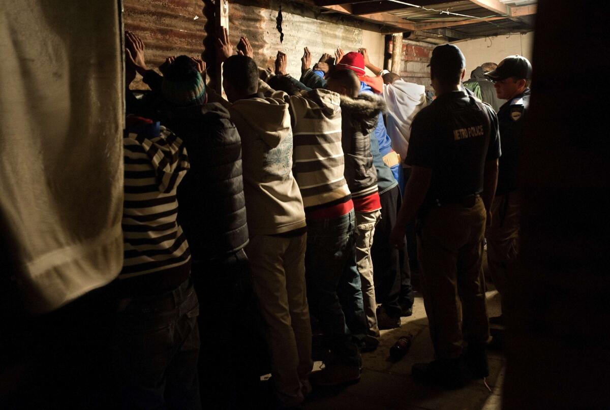 Men stand with their hands against a wall during a police raid in the Cape Town township of Manenberg in South Africa.