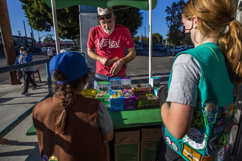 LOS ANGELES, CA - FEBRUARY 11: Chris Hillman, middle, buys Girl Scout Cookies from Madar Mee, 10, right, and Emma Diaz, 7, left, in the Mar Vista neighborhood at on Friday, Feb. 11, 2022 in Los Angeles, CA. (Francine Orr / Los Angeles Times)