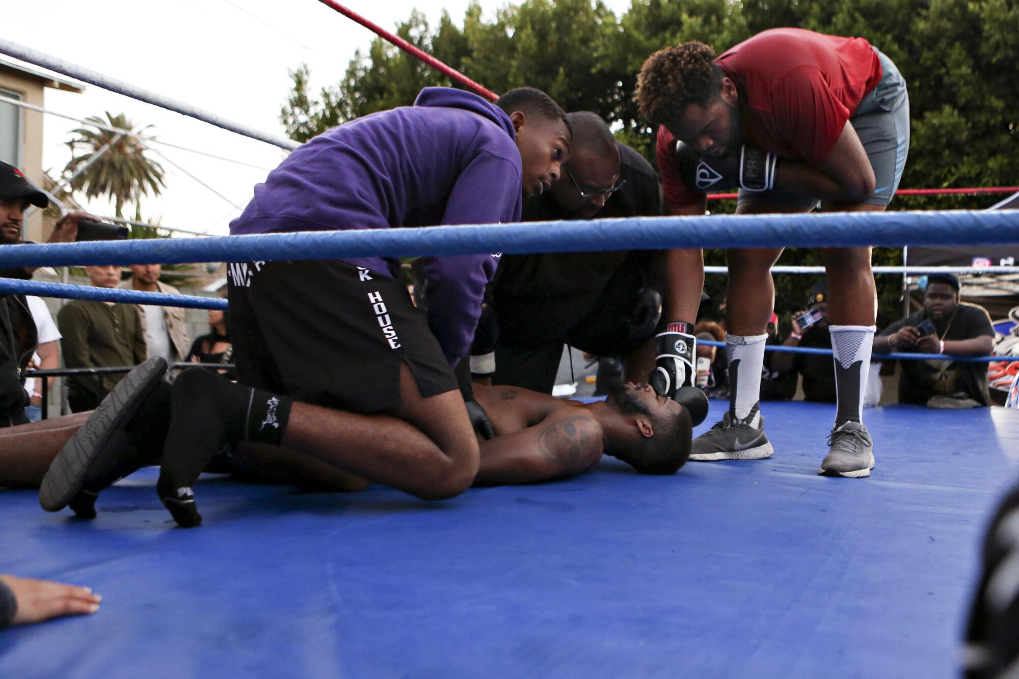 A man lies on the boxing ring mat as other men gather around him.