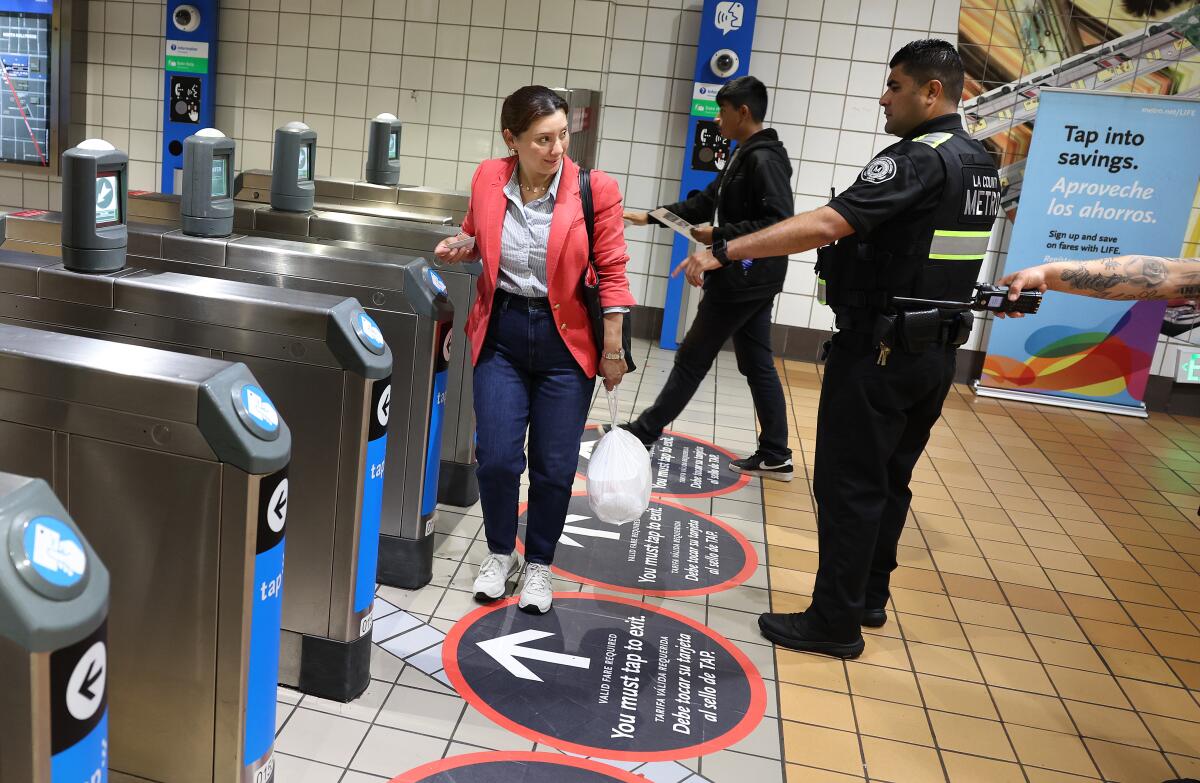 A uniformed security officer directs a transit passenger at a turnstile.