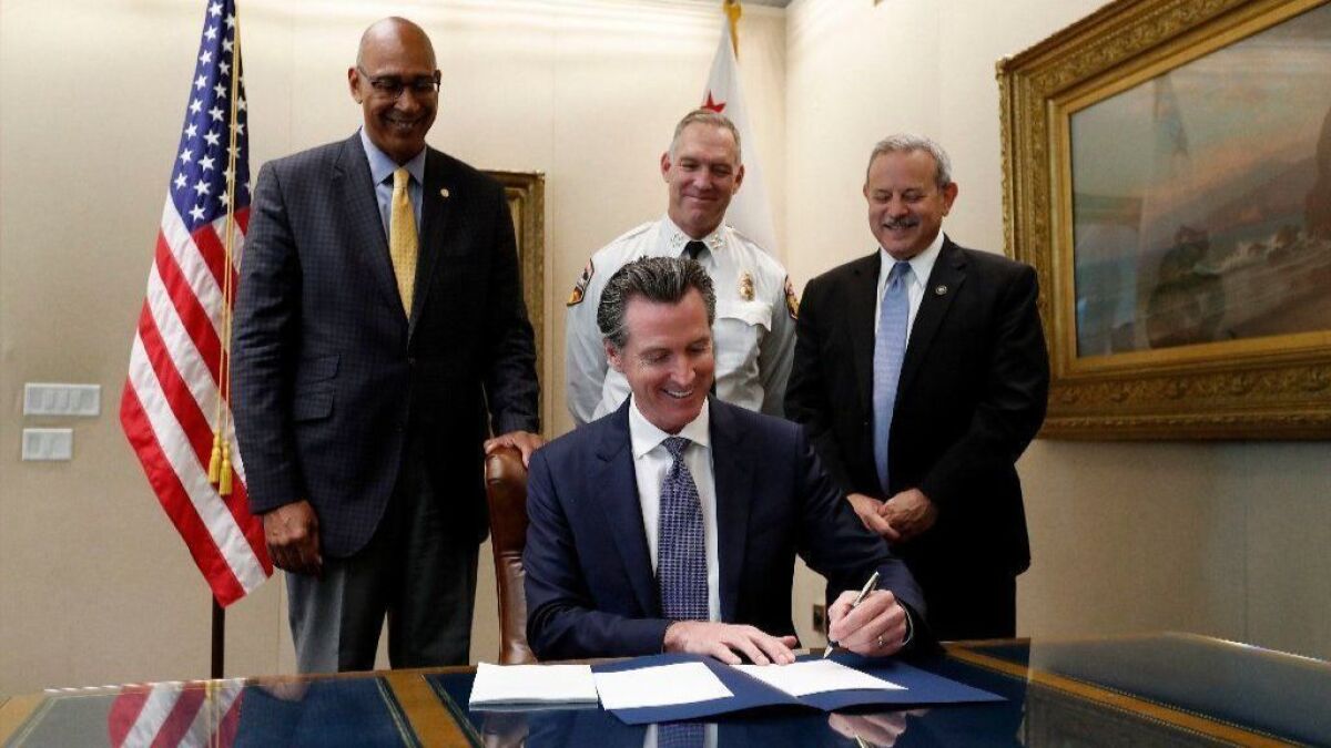 Gov. Gavin Newsom signs a bill to create a multibillion-dollar wildfire fund for utilities on Friday at the state Capitol.