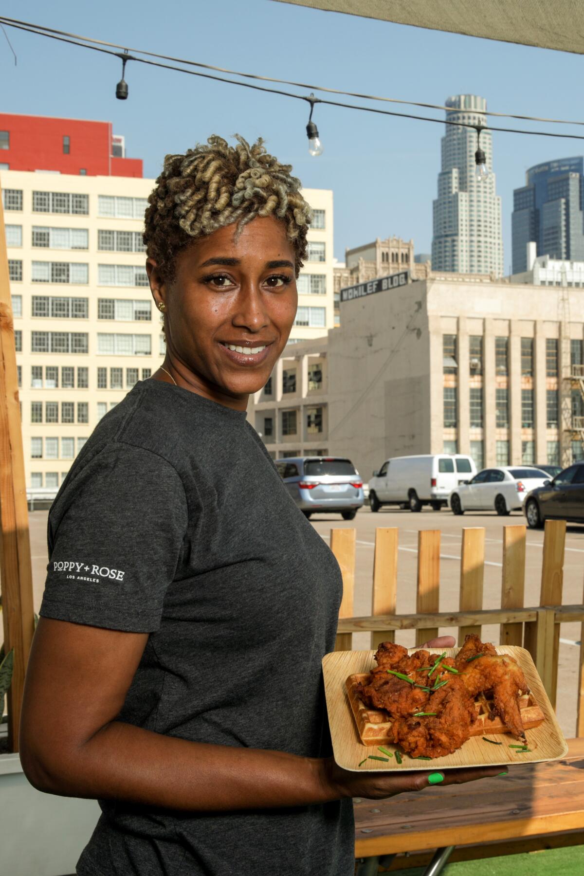 A woman holds a platter of fried food with a backdrop of downtown Los Angeles