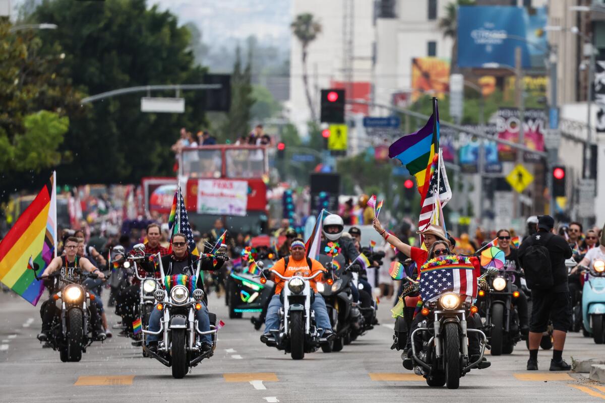 A group of motorcycle riders in the LA Pride Parade with flags.