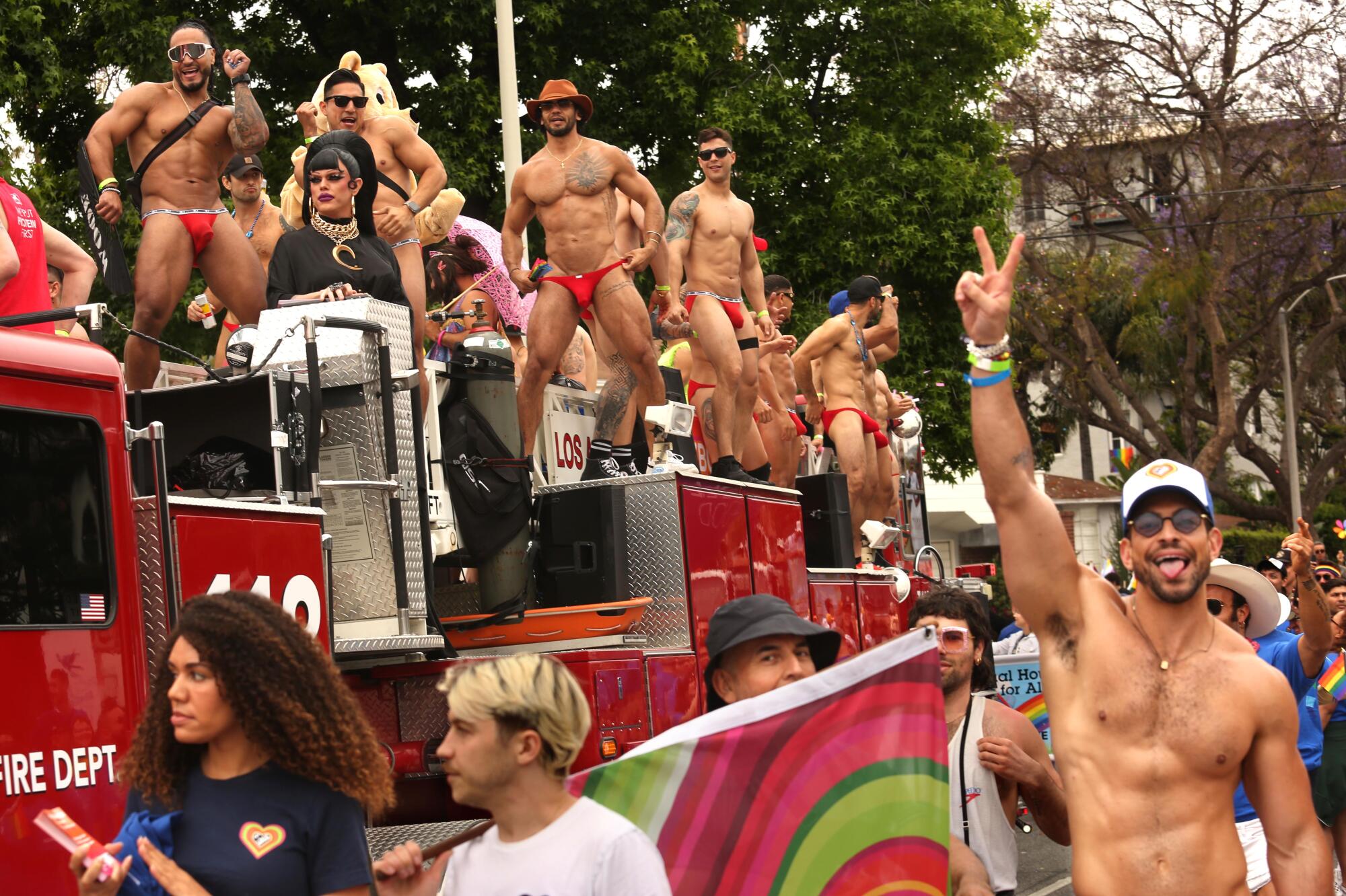 Muscular men in tiny red briefs atop a fire truck.