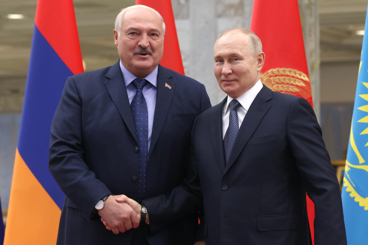 Belarus' President Alexander Lukashenko and Russian President Vladimir Putin shake hands in front of flags.