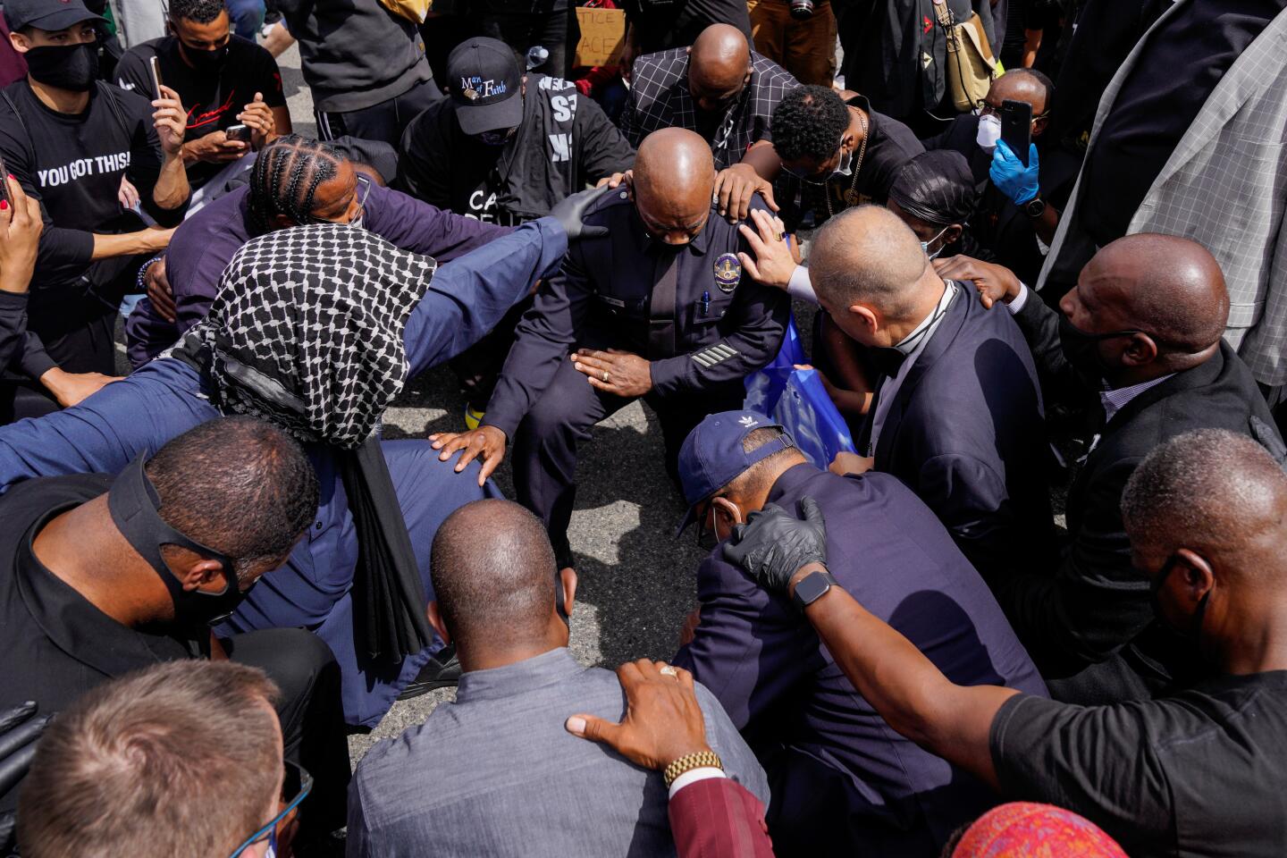 LAPD Cmdr. Gerald Woodyard takes a knee with protesters and L.A. clergy during a march in downtown Los Angeles on Tuesday.