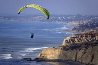 A paraglider soars along the San Diego coast with Flat Rock at Torrey Pines State Reserve.