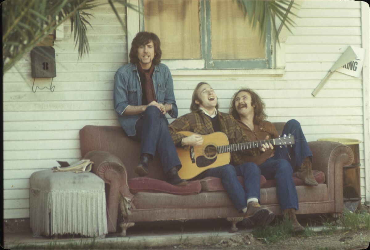 From left, Graham Nash, Stephen Stills and David Crosby sing on a couch on a porch in 1969.