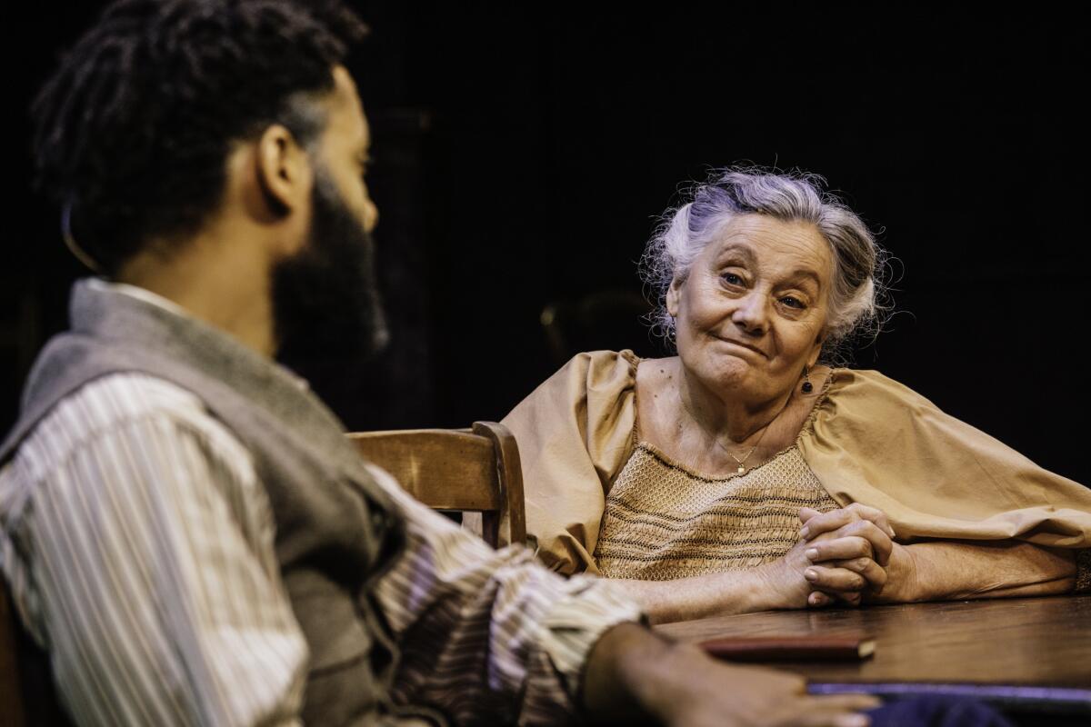 An older woman looks at a man in profile onstage.