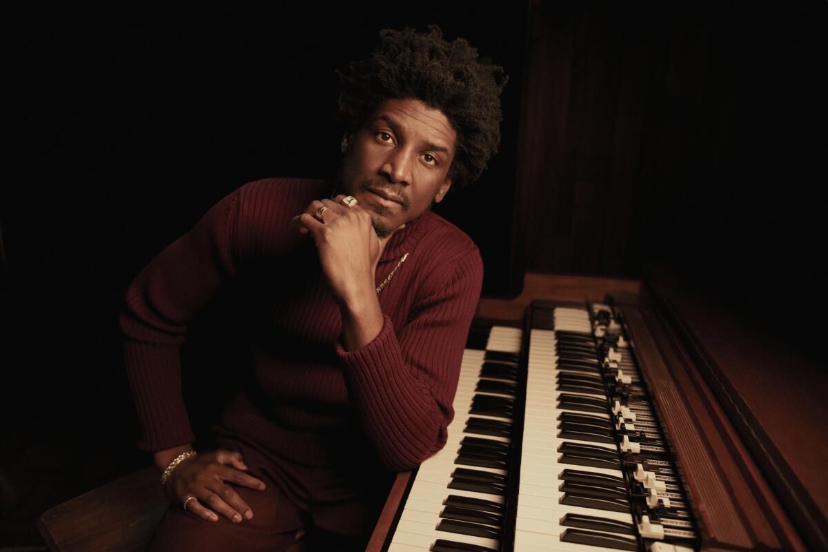 A young composer in a dark room, leaning his chin on his hand and his elbow on an organ keyboard.