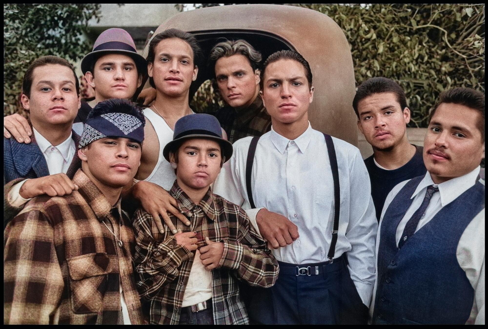 The actors who comprise the Vatos Locos gang pose in pachuco and cholo attire in front of a rusted-out pickup truck.
