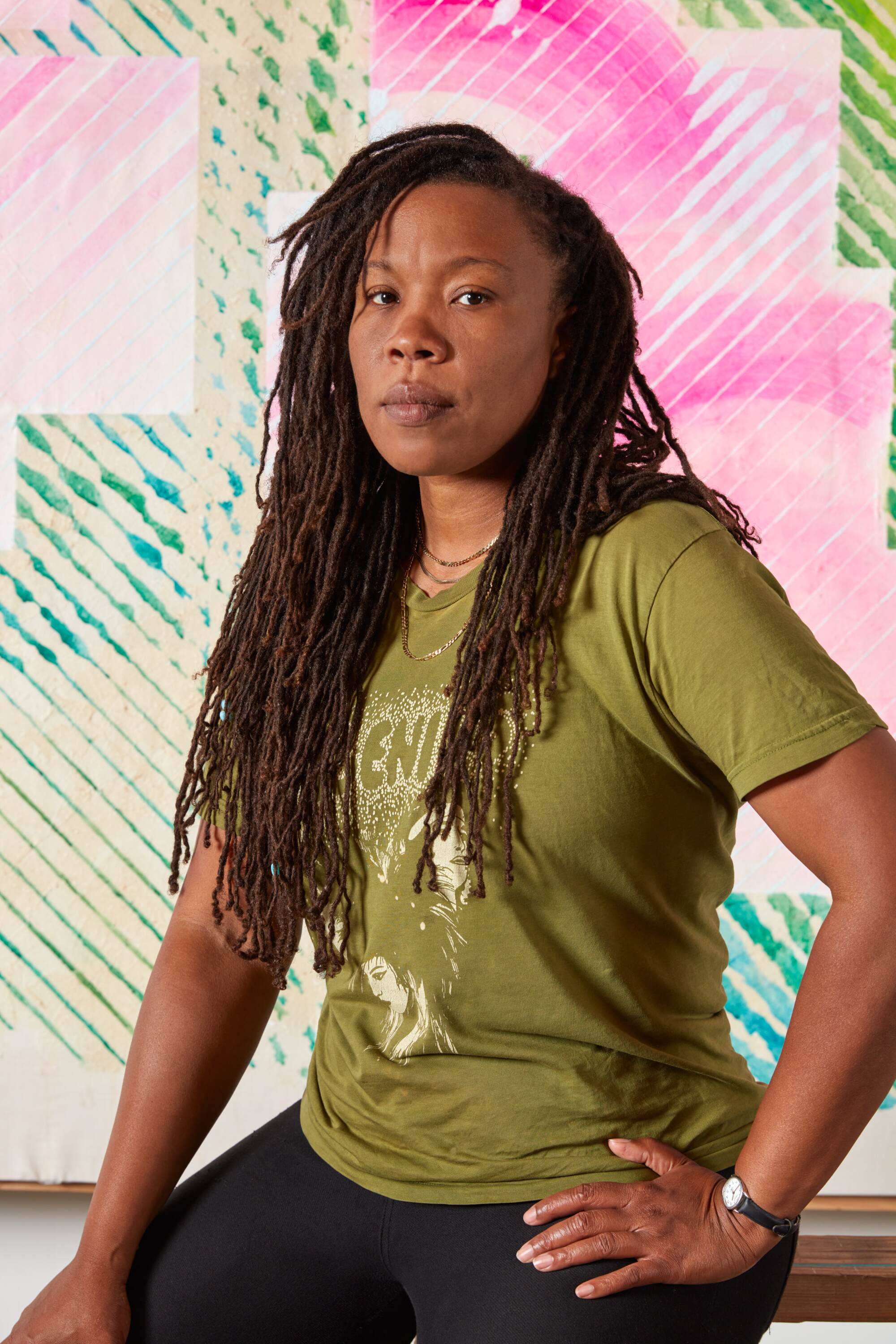 Tomashi Jackson poses in a green T-shirt in front of one of her abstract artworks.