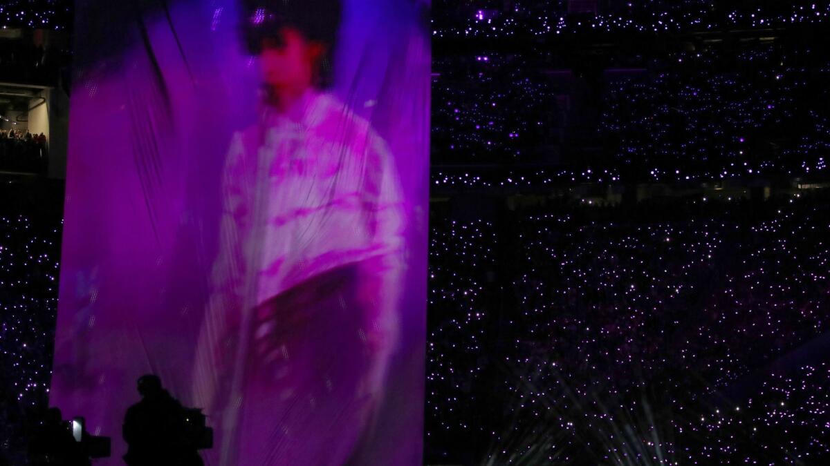 Justin Timberlake performs onstage while a large image of Prince is projected next to him.