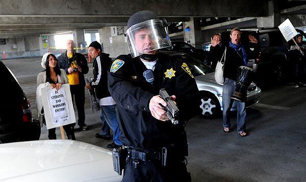 A University of California police officer draws his gun as protesters gather outside a UC regents meeting. Police said he had been struck on the head.