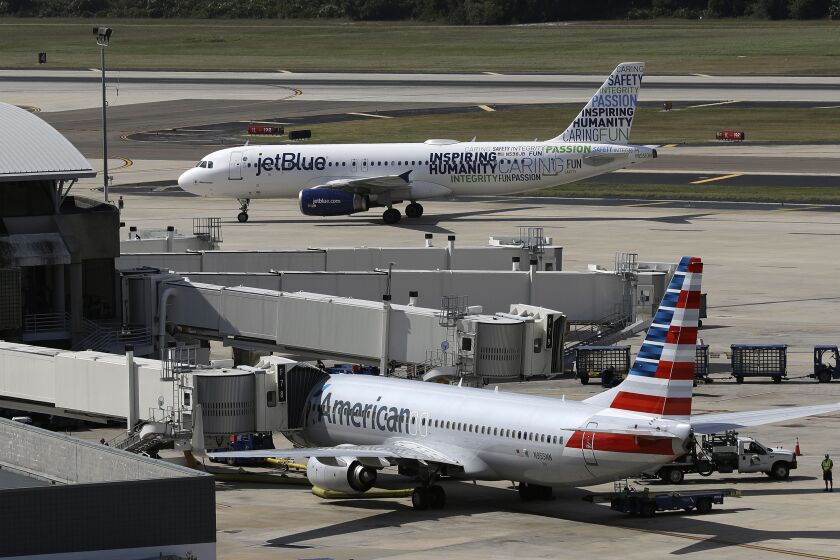 FILE - A JetBlue Airbus A320 taxis to a gate Wednesday, Oct. 26, 2016, after landing, as an American Airlines jet is seen parked at its gate at Tampa International Airport in Tampa, Fla. The government is getting its day in court to try to block a partnership between American Airlines and JetBlue. A trial is scheduled to start Tuesday, Sept. 26, 2022 in the Justice Department's antitrust lawsuit against the airlines. (AP Photo/Chris O'Meara, File)