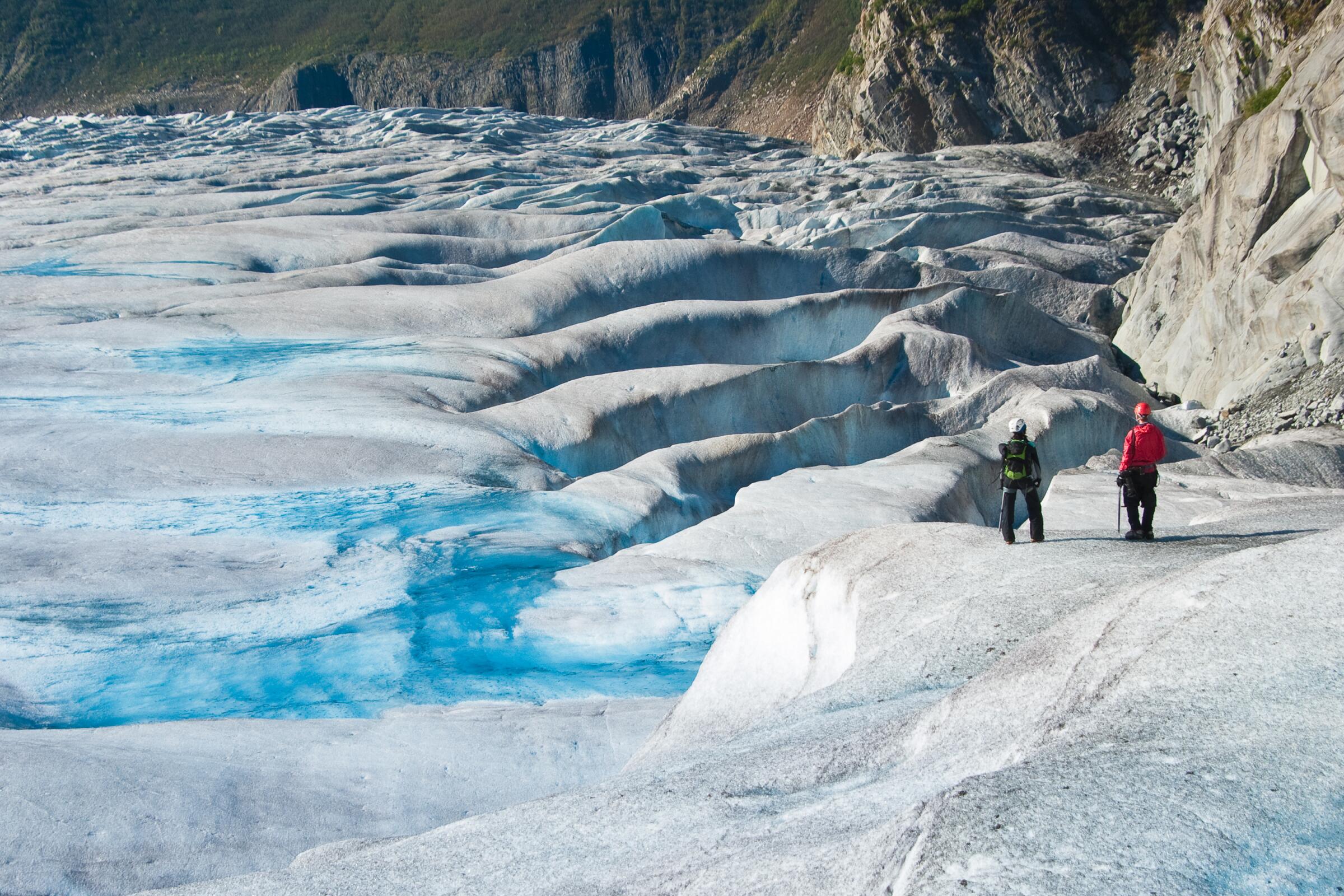 Two people stand on a glacier.   