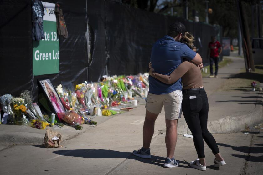 ARCHIVO - Dos personas que conocían a una víctima no identificada de un incidente fatal en el concierto Astroworld se abrazan el domingo 7 de noviembre de 2021 frente a un memorial improvisado en Houston. Las familias de dos amigos de Illinois que murieron en el concierto demandaron por homicidio culposo al rapero Travis Scott, la compañía de entretenimiento Live Nation y otros. (AP Foto/Robert Bumsted, Archivo)