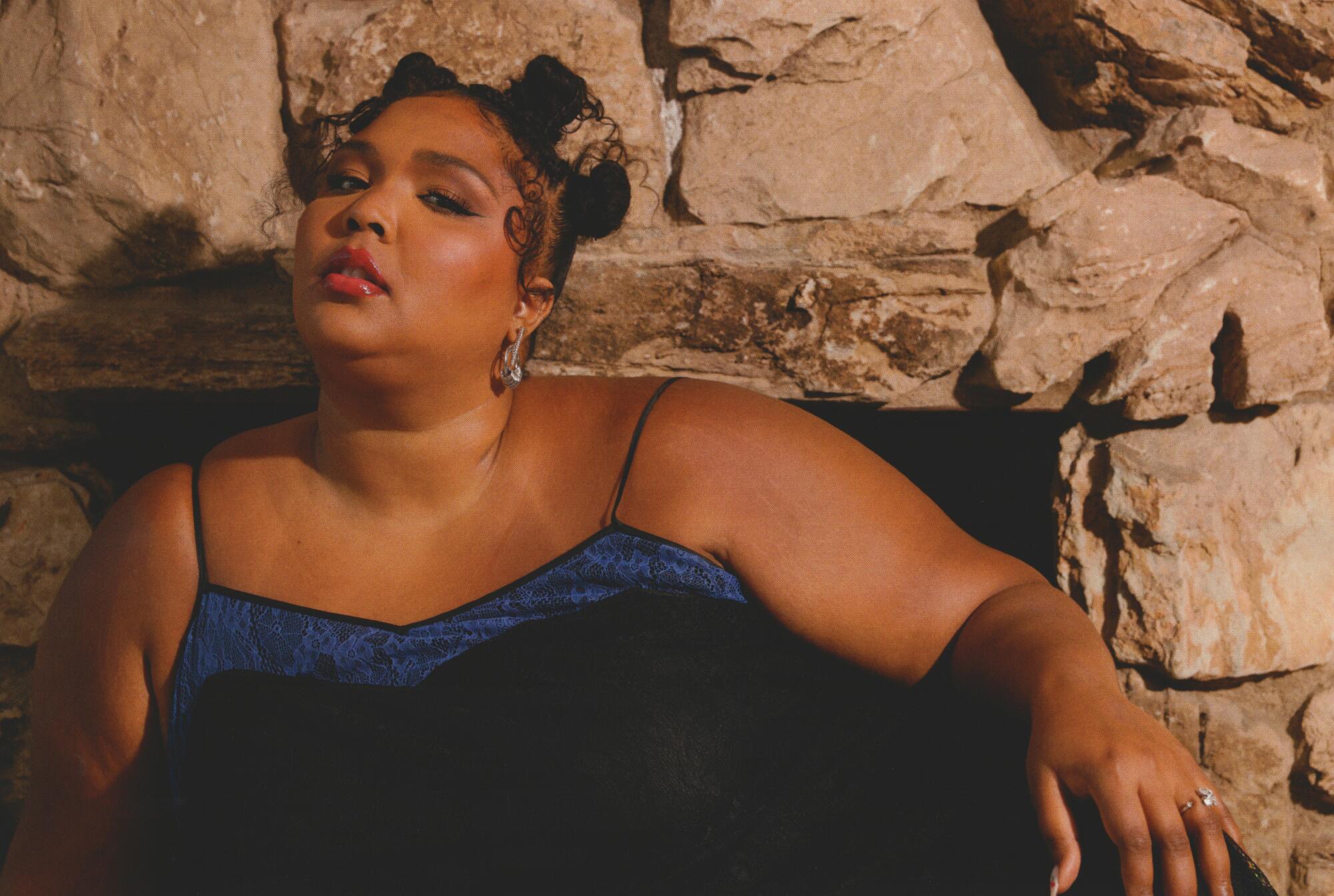 A woman in a black dress leans against a rock-walled fireplace