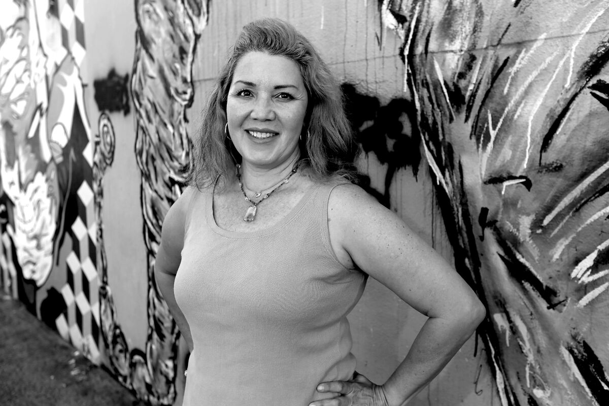 A woman smiles in front of a floral-painted wall