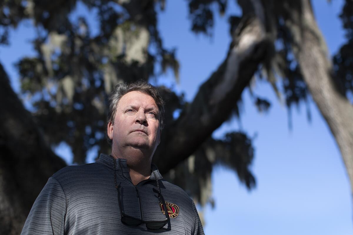 A man stands under a grove of trees