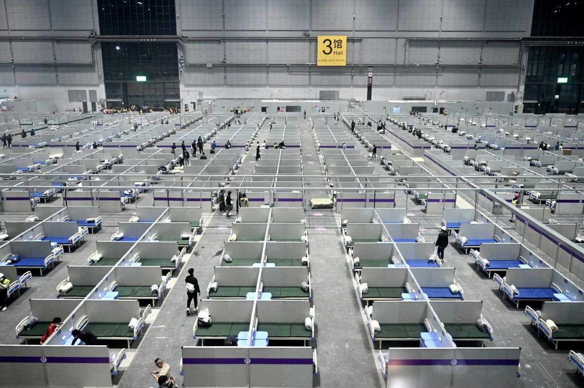 A view of neat rows of hospital beds in a cavernous warehouse setting.