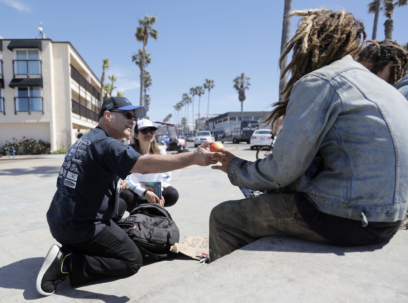 Doors of Change founder and president Jeffrey Sitcov, gives an apple to a youth on the seawall at Ocean Beach.