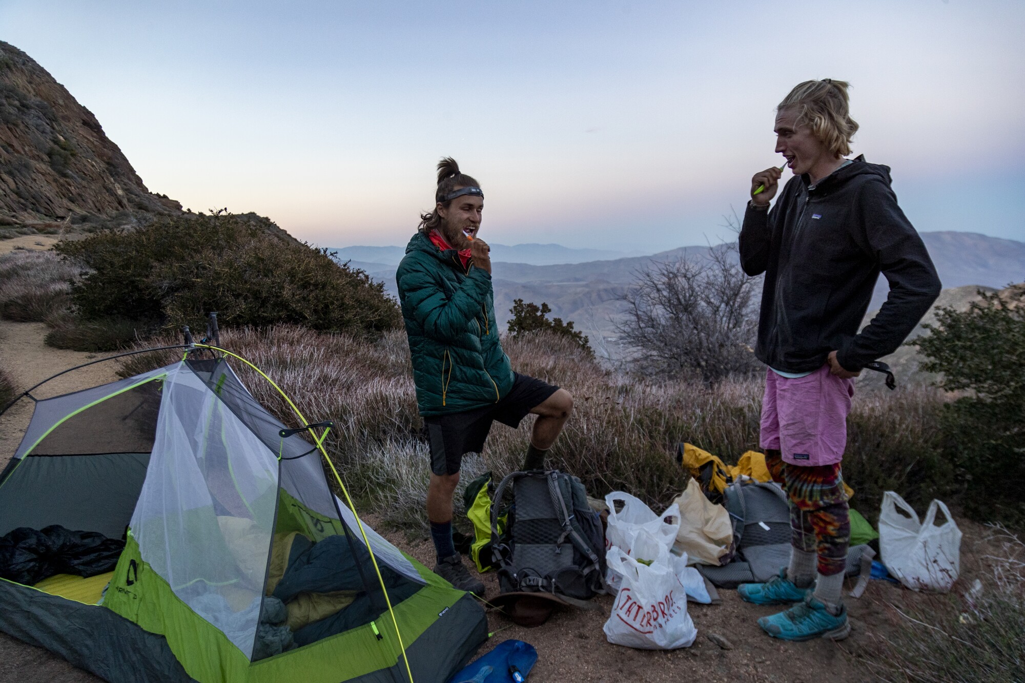 Two men brush their teeth outside a tent.