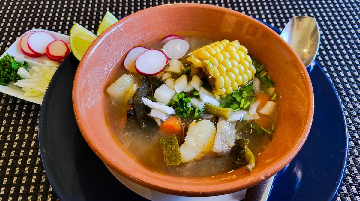 A bowl of clear broth soup teeming with vegetables.