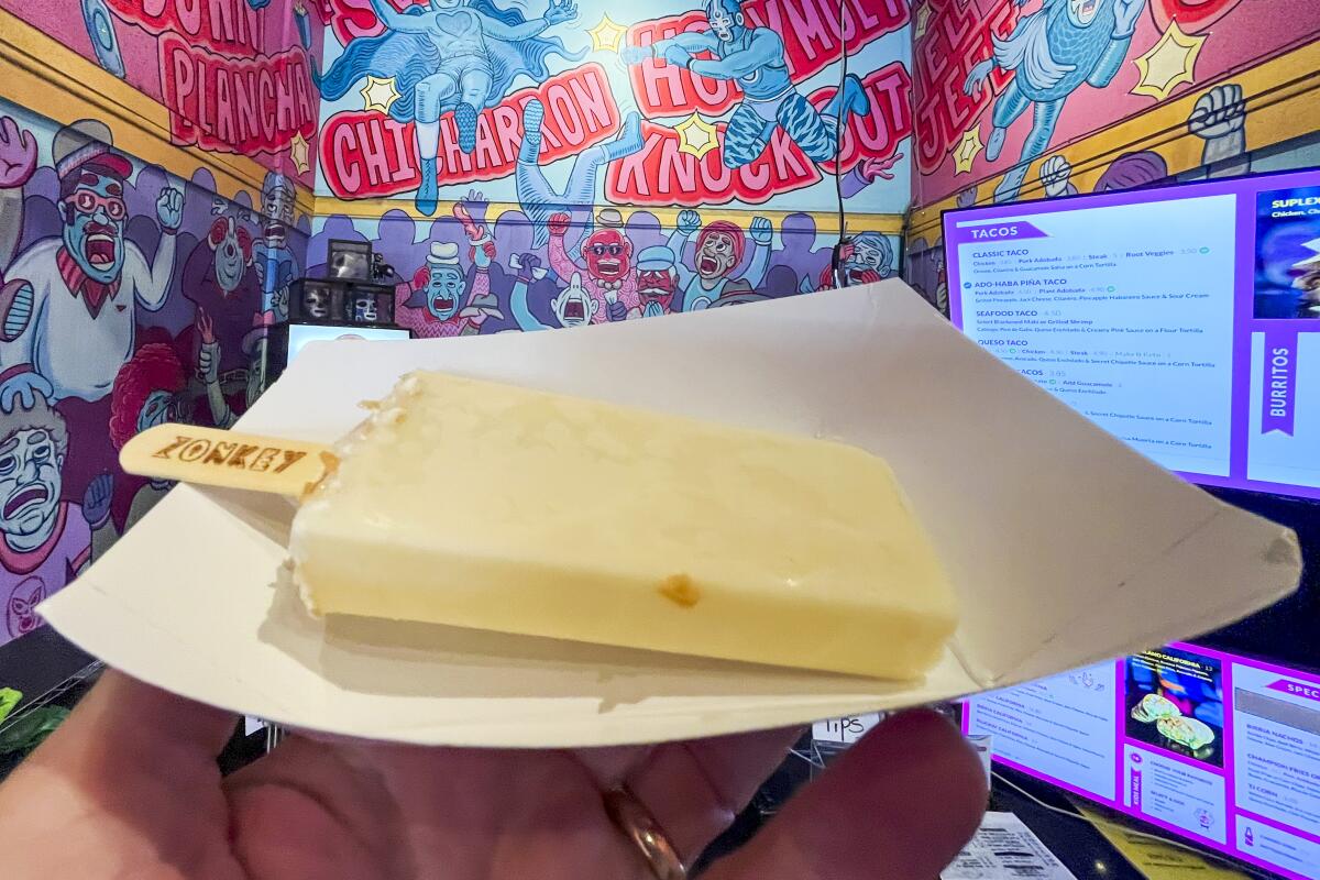 A white popsicle on a cardboard tray, held up in front of a colorfully decorated wall