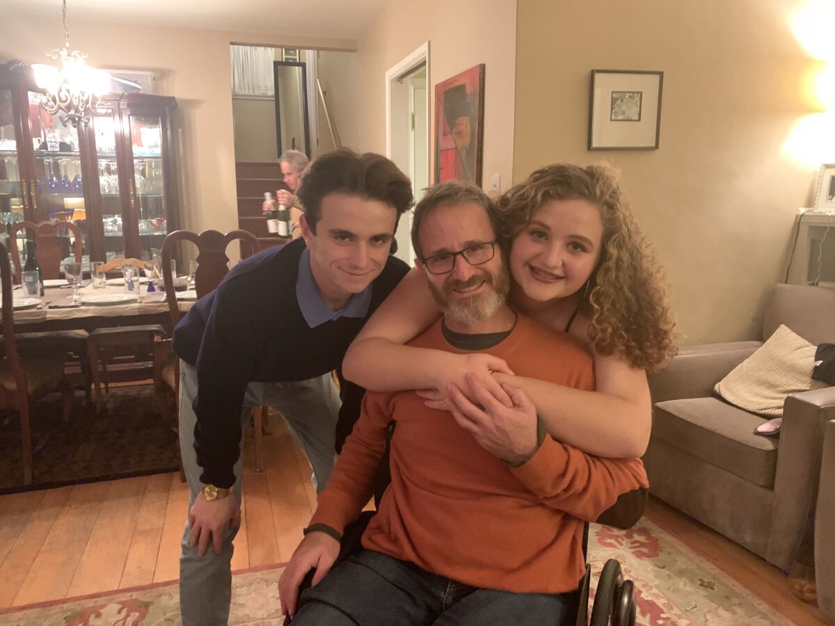 Sam Kolb in a wheelchair being hugged by his 15-year-old daughter and next to his then 18-year-old son in November 2019 