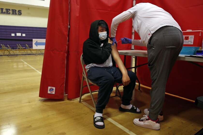 California unveils sweeping plan for full reopening on June
15 as COVID-19 fades 2 LOS ANGELES, CA - MAY 17: Nedvel Ventura, 16, is vaccinated with Pfizer by Barbie Varragan, right, at the Manual Arts High School basketball and gym building in downtown on Monday, May 17, 2021 in Los Angeles, CA. The school is one of 200 sites that the Los Angeles Unified School District has deployed mobile vaccination teams to get as many shots into students' arms as possible. (Dania Maxwell / Los Angeles Times)