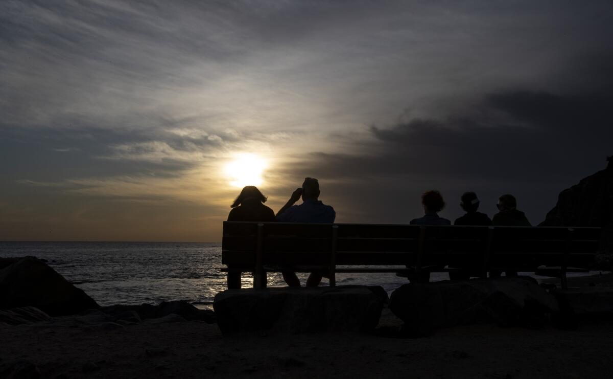 Two people sit on a bench watching the sunset in Dana Point.