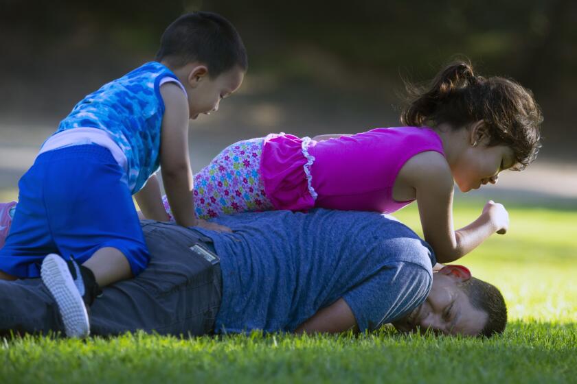 Los Angeles, CA JUNE 21, 2020: Samuel Rodas, 40, bottom, plays with his son Adrian Rodas, age 2, left, and daughter Karla Rodas, 4, right, on Father's Day in Griffith Park, CA in Los Angeles, CA June 21, 2020. Samuel was helping his son play in the tree. (Francine Orr/ Los Angeles Times)