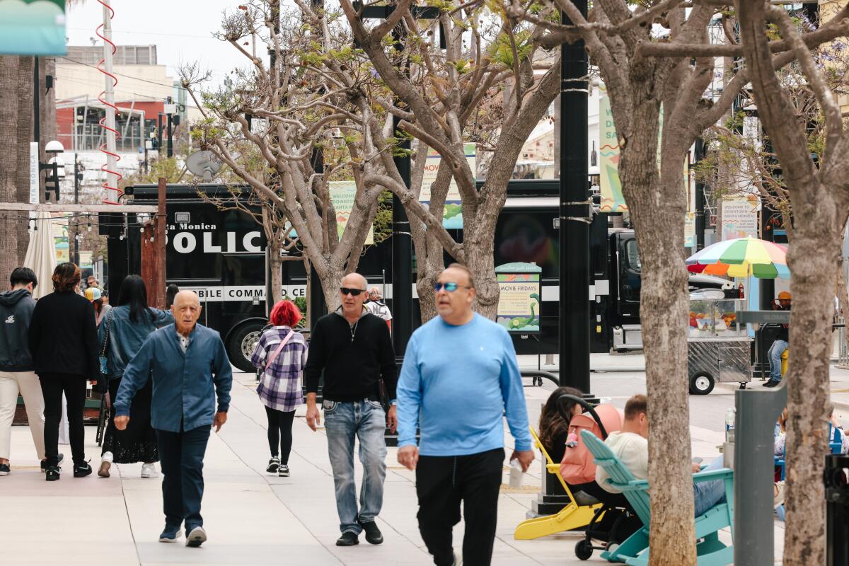 People walk near a police van in the Third Street Promenade.