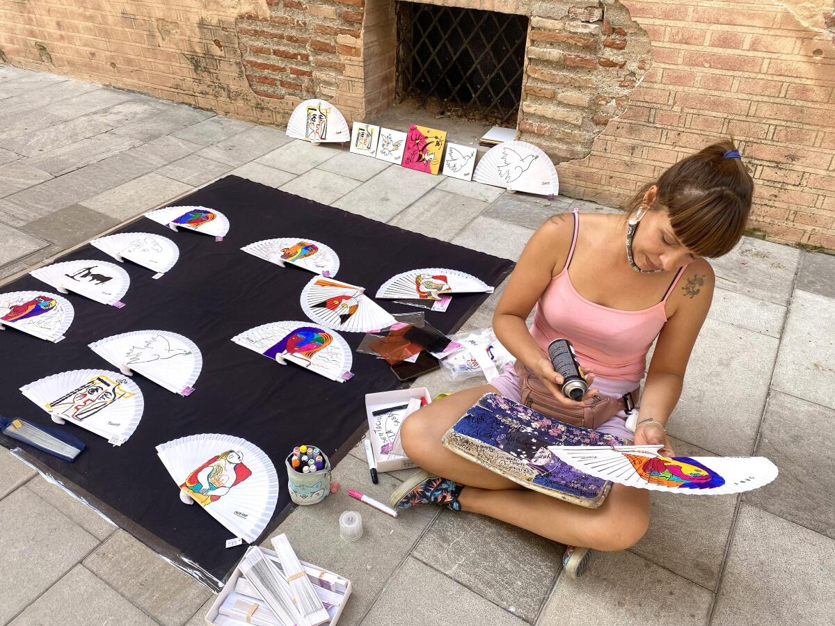 A woman sits on the ground while crafting souvenir fans
