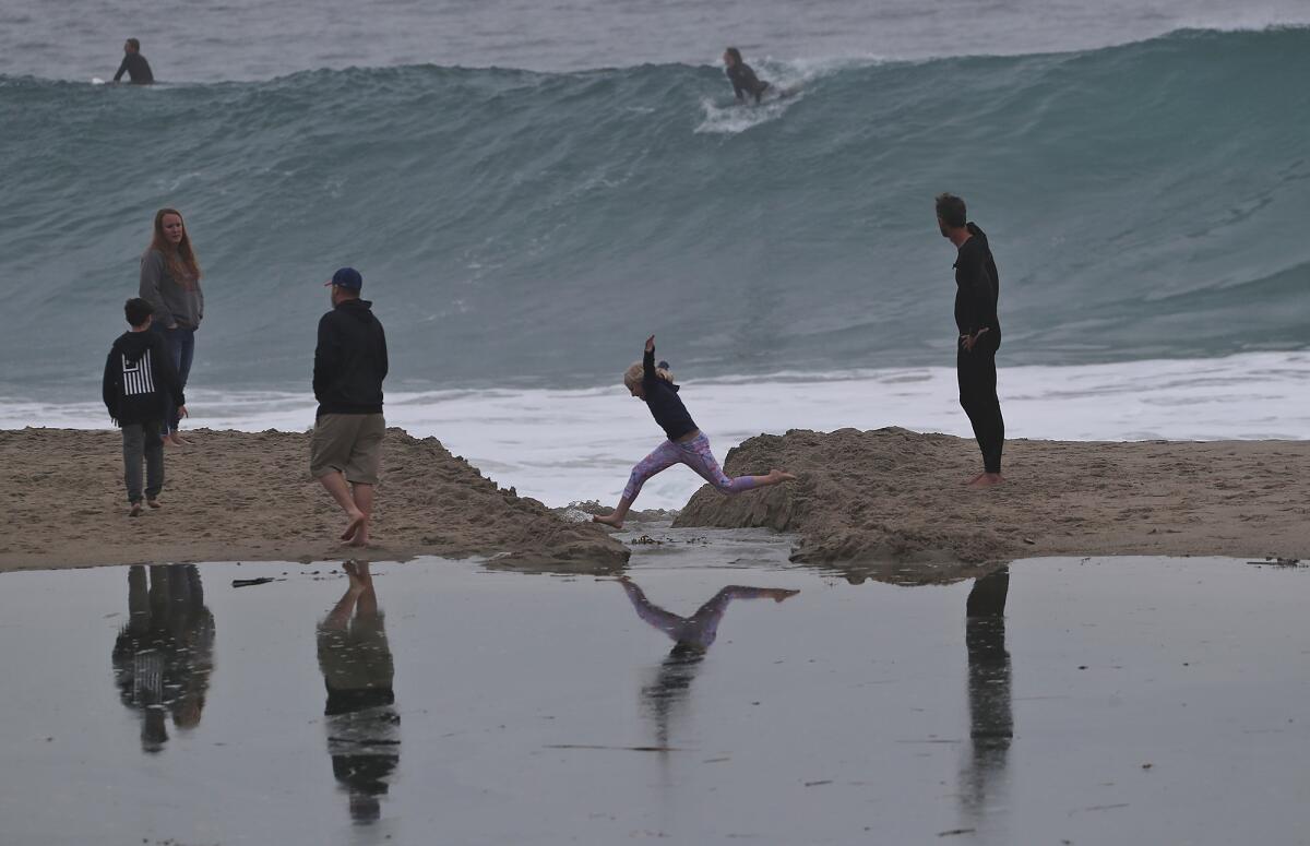 Visitors jump over a break in the puddle formed in the sand as a light rain begins to fall at Aliso Beach Park.