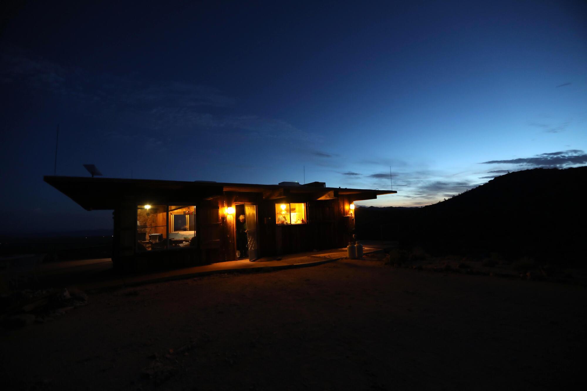 Lights glow in a house as night falls on the desert.