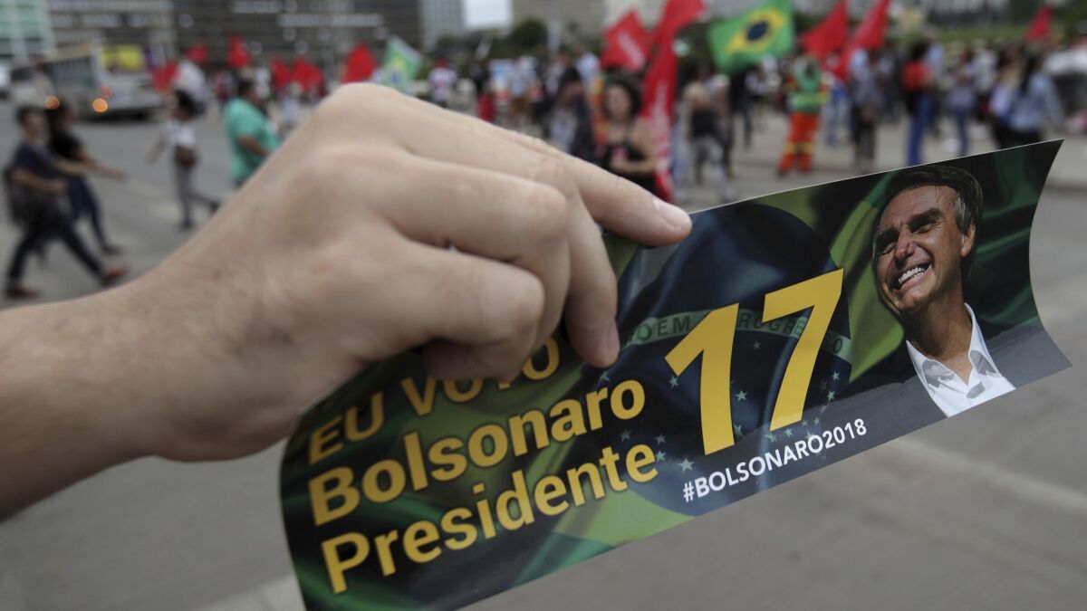 A supporter of presidential front-runner Jair Bolsonaro holds up a bumper sticker promoting her candidate during a campaign rally in Brasilia, Brazil, Wednesday.
