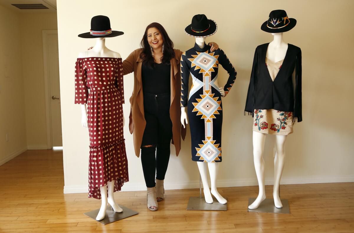 Crow and Northern Cheyenne fashion designer Bethany Yellowtail is photographed with three of her designs, from left, a women's elk tooth-print dress, a sun road women's dress and a leather fringe cape, on display at her studio in Valley Village on Jan. 11, 2017.