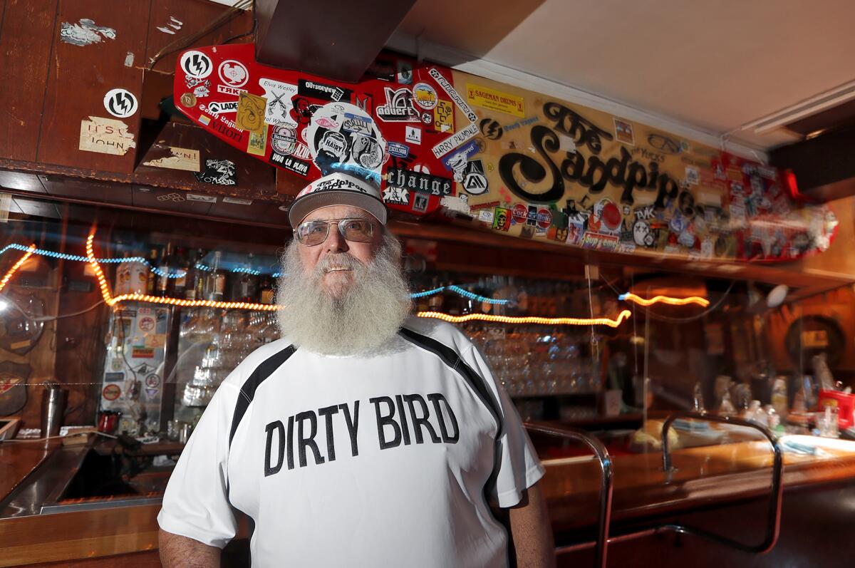 Longtime owner Chuck Harrell stands under the surfboard at the Sandpiper Lounge, also known to locals as the "Dirty Bird."