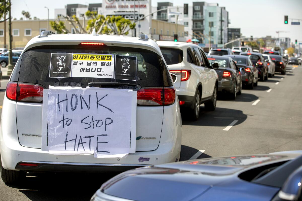 A car caravan drives down a street with a sign that reads "Honk to stop hate" on the back of one of the cars. 
