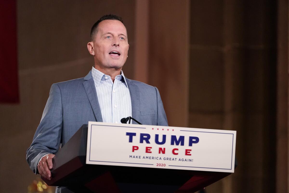 Richard Grenell speaking on a stage from a lectern with a Trump-Pence campaign sign