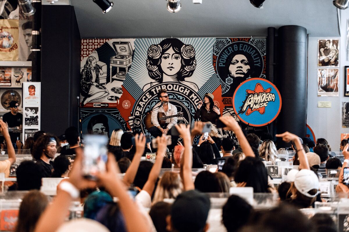 Fans hold up their cell phones as they watch two musicians on a stage at a record store.