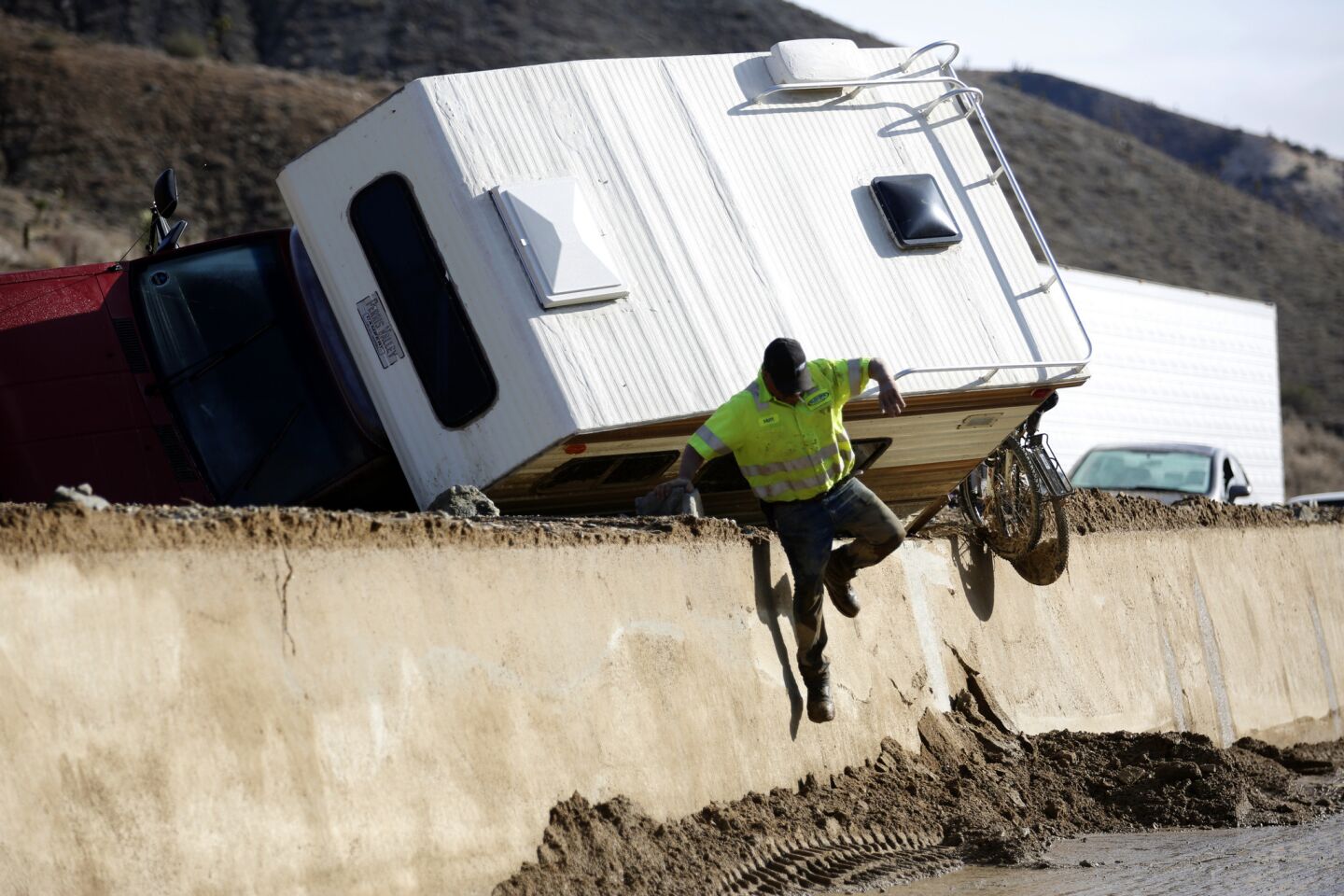 Gary Lumpkins of Golden Empire Towing jumps down a high cement barricade on California 58 east of Tehachapi where up to 20 feet of mud and debris pummeled the area earlier in the week and forced drivers to flee.