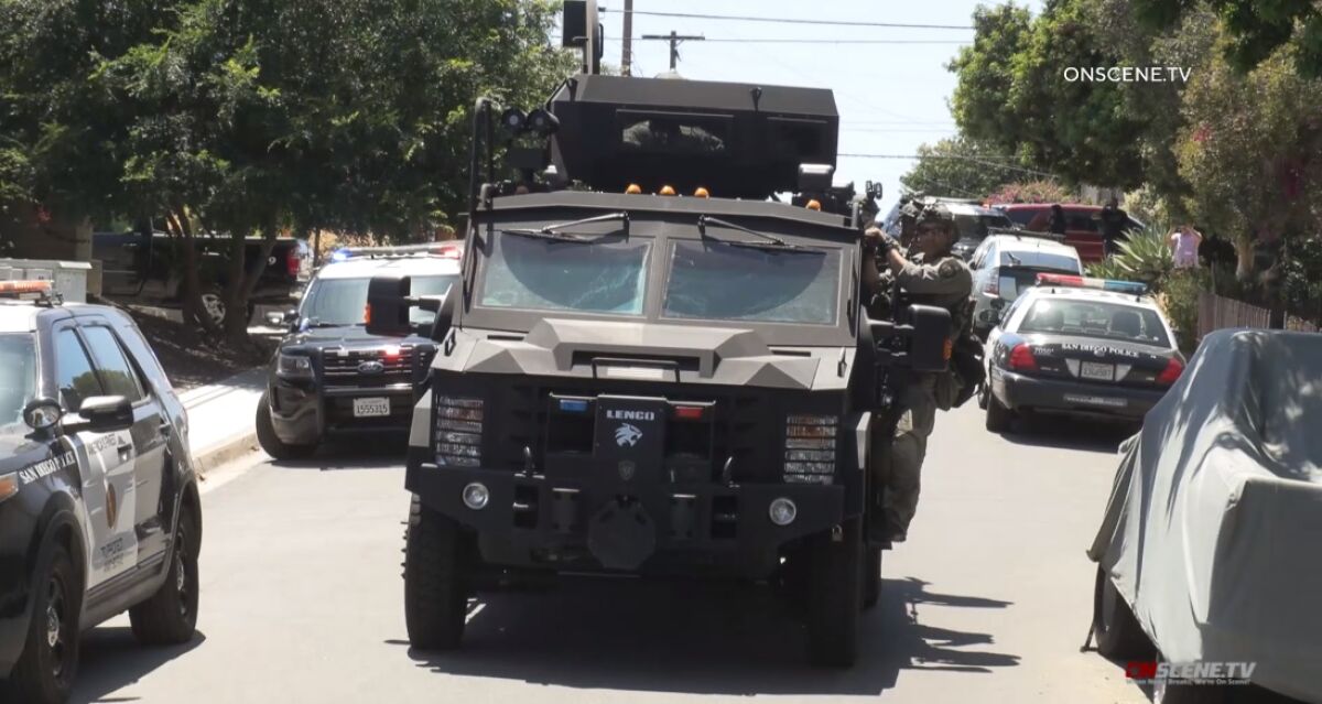 San Diego SWAT officers ride on the side of an armored vehicle Friday afternoon while responding to a standoff in North Park.