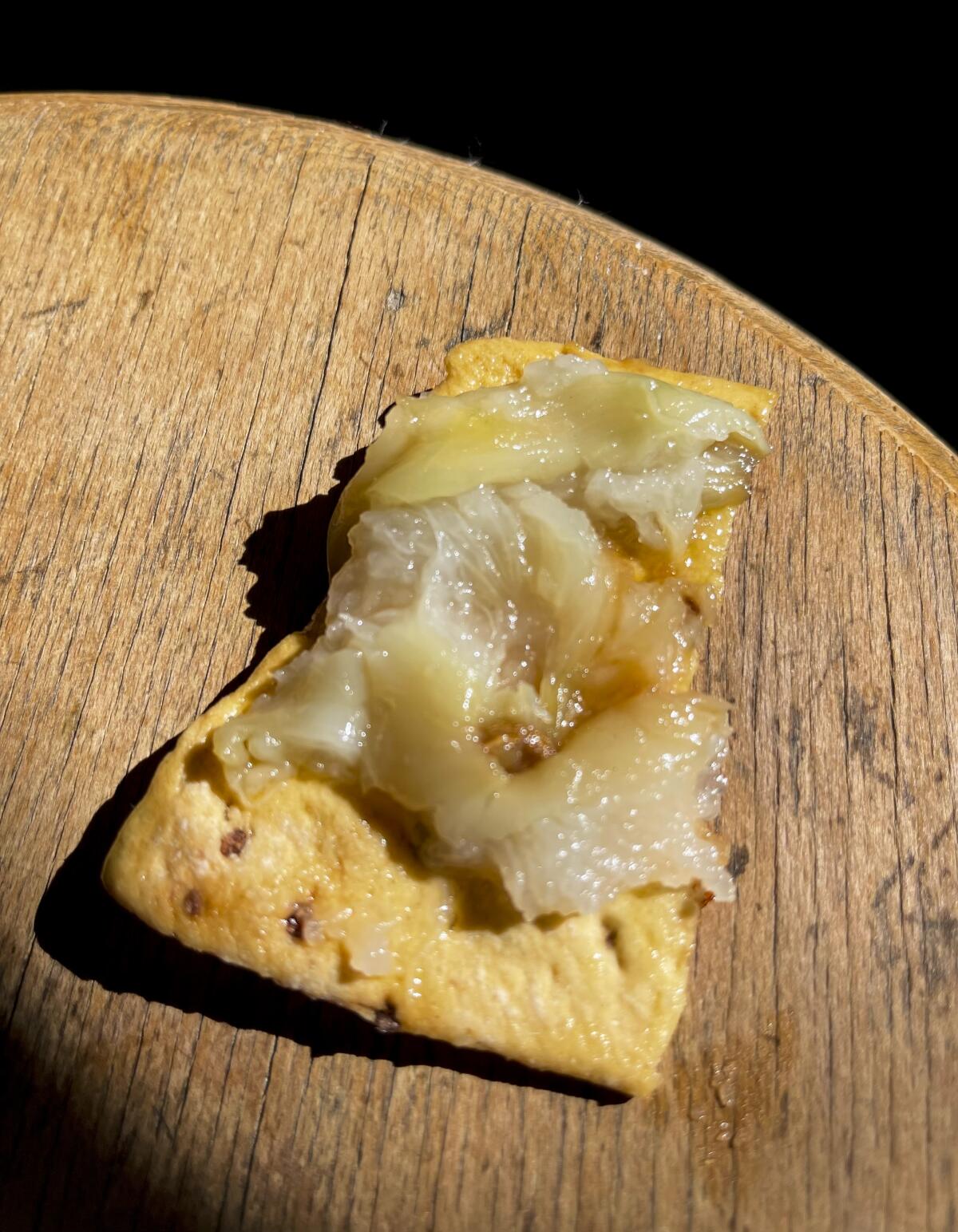 Closeup of a cracker spreaded with soft garlic.