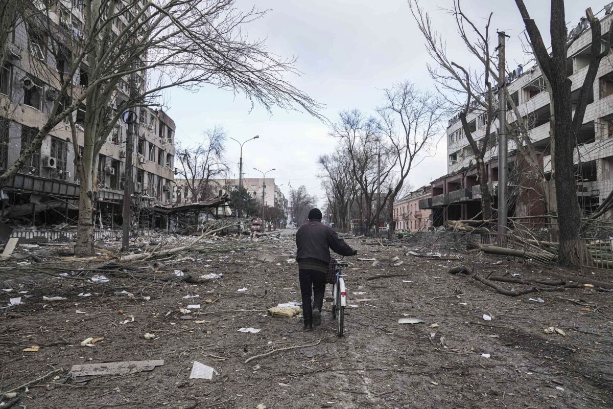 FILE - A man walks with a bicycle in a street damaged by shelling in Mariupol, Ukraine, March 10, 2022. In talks between Russia and Ukraine toward a possible cease-fire after three weeks of intense fighting, negotiators are exploring prospects of possible “neutrality” for Ukraine. (AP Photo/Evgeniy Maloletka, File)