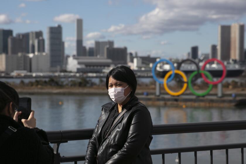 FILE - In this Jan. 29, 2020, file photo, a tourist wearing a mask poses for a photo with the Olympic rings in the background, at Tokyo's Odaiba district. Tokyo Olympic organizers repeated their message at the start of two days of meetings with the IOC: this summer's games will not be cancelled or postponed by the coronavirus spreading neighboring China. (AP Photo/Jae C. Hong, File)