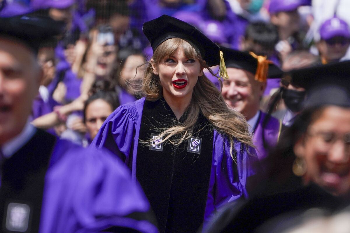 A blond woman wearing a velvet black graduation cap and purple graduation gown in a crowd